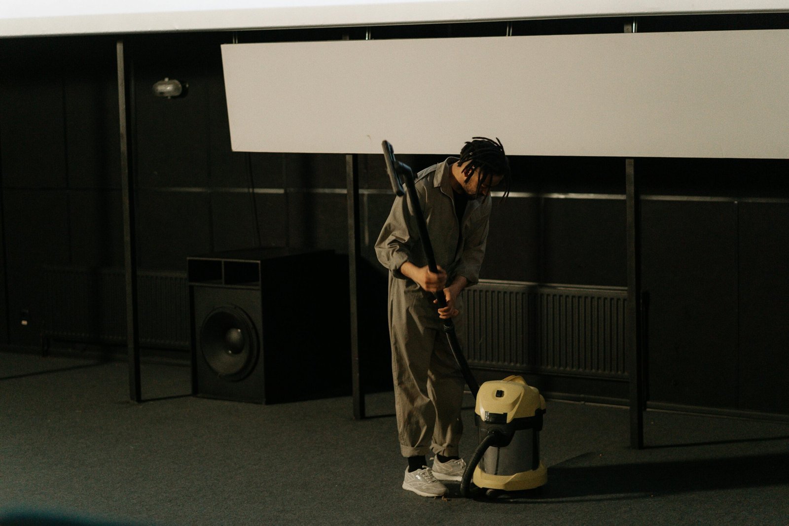 A person in uniform using a vacuum cleaner inside an auditorium with a visible speaker.